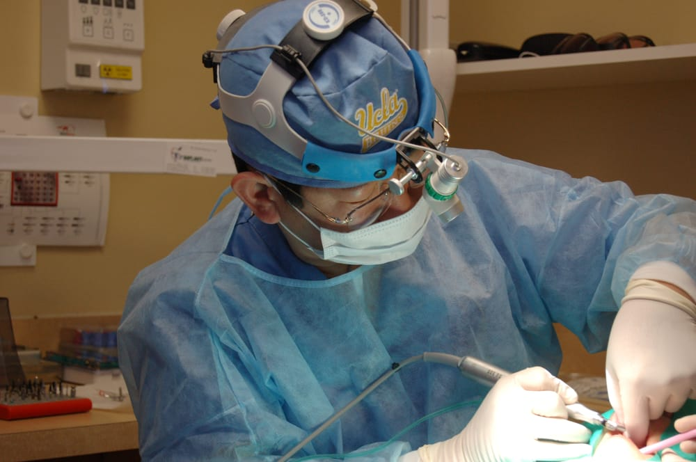 Dr. Andre Lee performing a dental procedure while wearing surgical attire, magnifying loupes, and a headlight